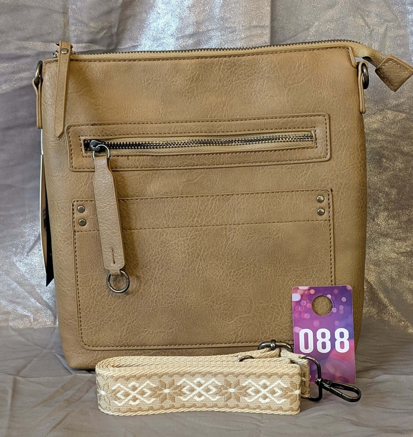 Tan crossbody bag with pattern strap featuring multiple zip pockets and a sleek design.